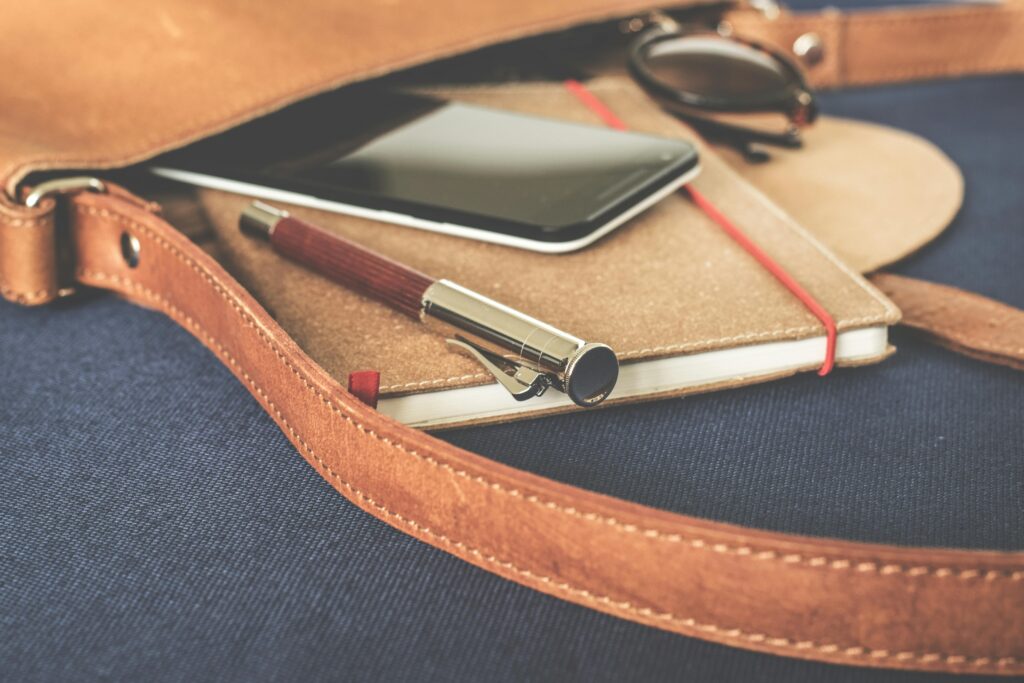 a bag on its side on a desk with a notebook, pen, and phone coming out of it