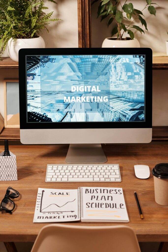 a computer screen with the words digital marketing written on it, a keyboard, and an open notebook in front of it